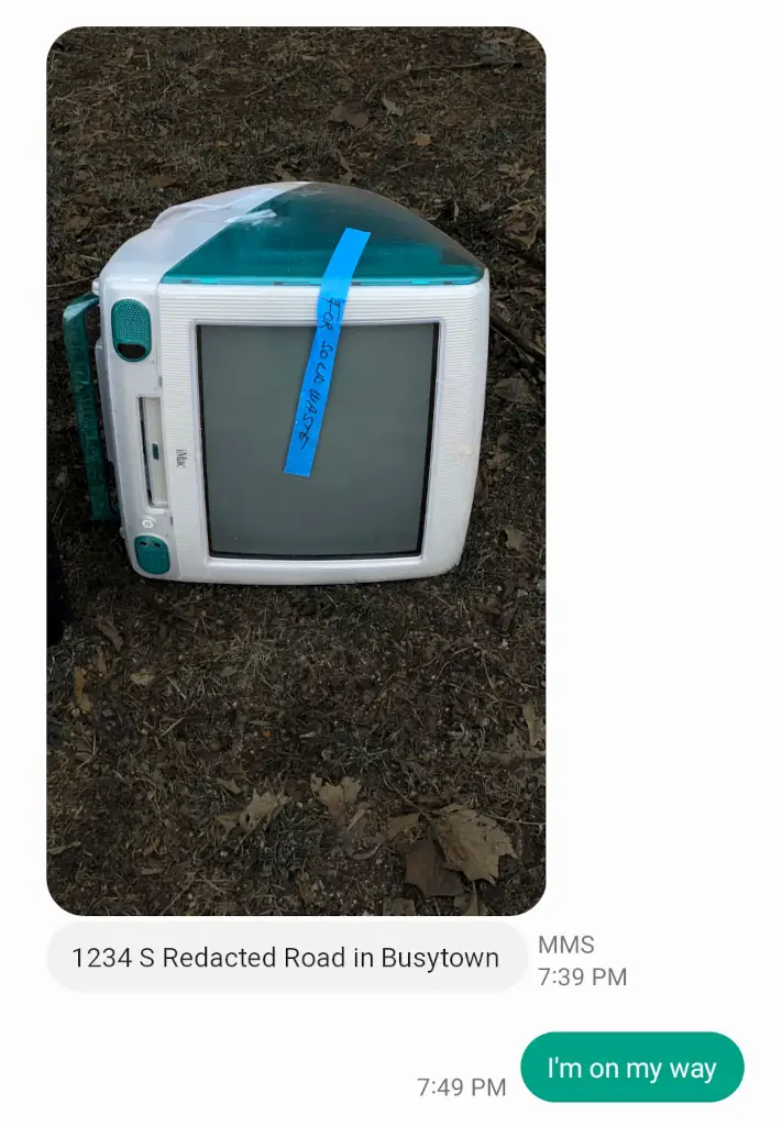 An SMS conversation.

In the first message, a Bondi Blue iMac G3 (large translucent 90s all-in-one computer) lies on its side in brown grass. It has tape on it that says "for solid waste". The message also includes an address: 1234 S Redacted Road in Busytown.

The second message (a reply) is a simple "I'm on my way".