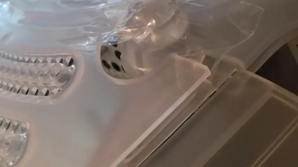 A closeup of the underside of an iMac G3 (translucent computer parts), with packaging tape holding parts of it together.
