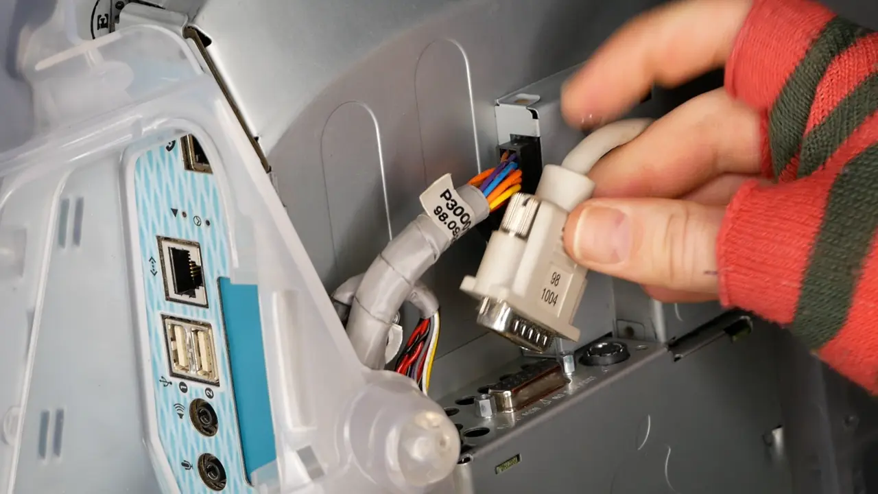 A hand plugging a monitor cable into an iMac G3 logic board.