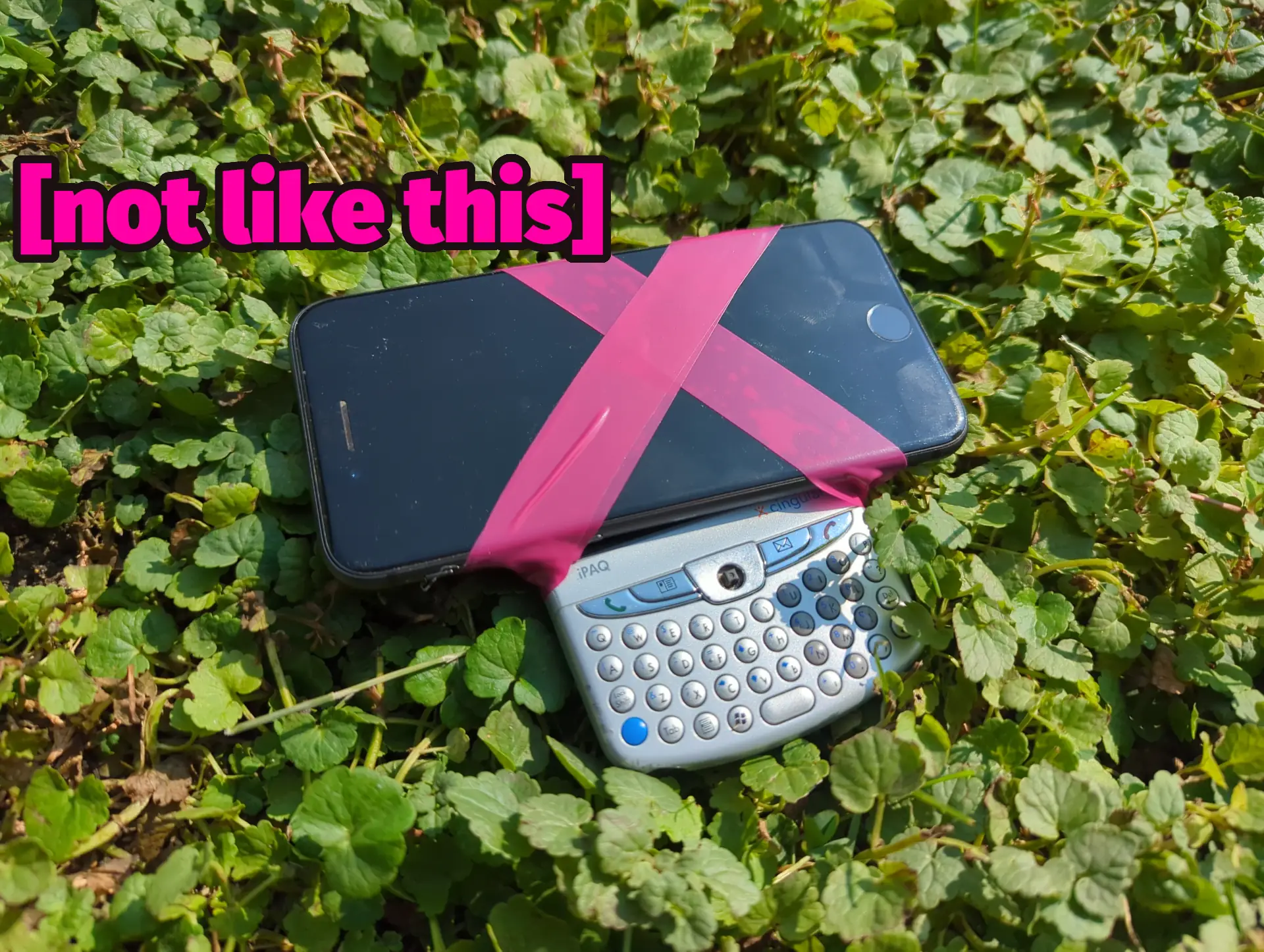 It's a smartphone taped to an older BlackBerry-style phone. The phones are sitting in a field of clover and superimposed are the words "[not like this]".